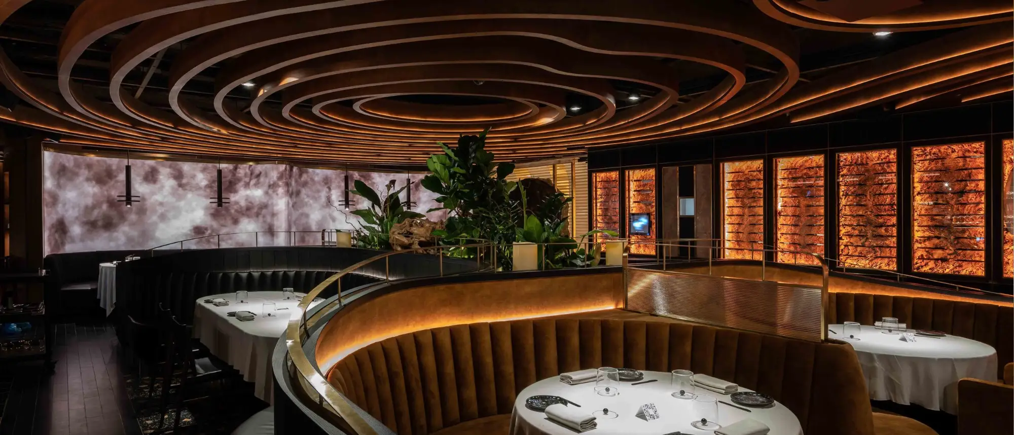 The award-winning sculptural interior of Leña Marbella restaurant inside the Puente Romano Beach Resort, featuring dramatic concentric wooden ceiling designs and elegant curved leather booths