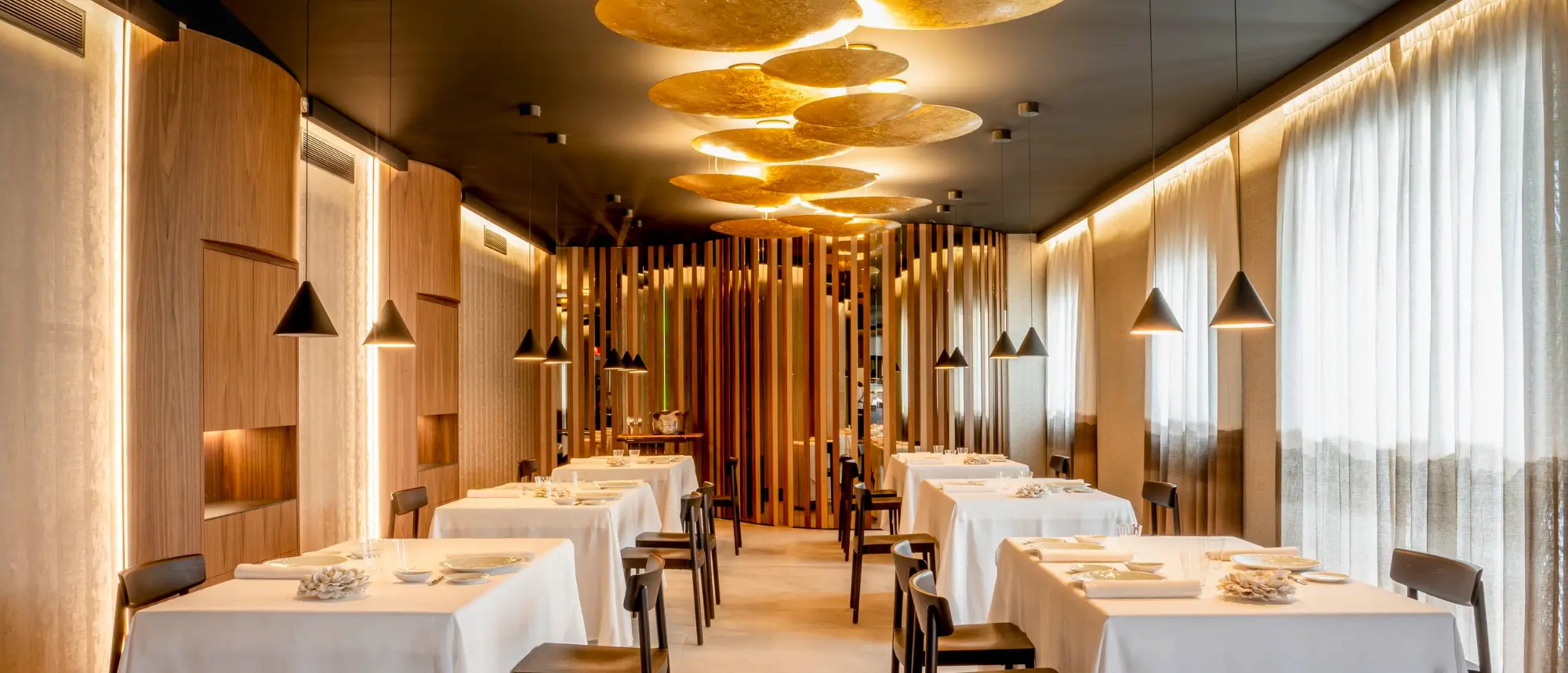The sophisticated, warm dining room of the two-Michelin-starred Restaurante Skina on the Marbella Golden Mile, featuring intimate tables and gold ceiling installations